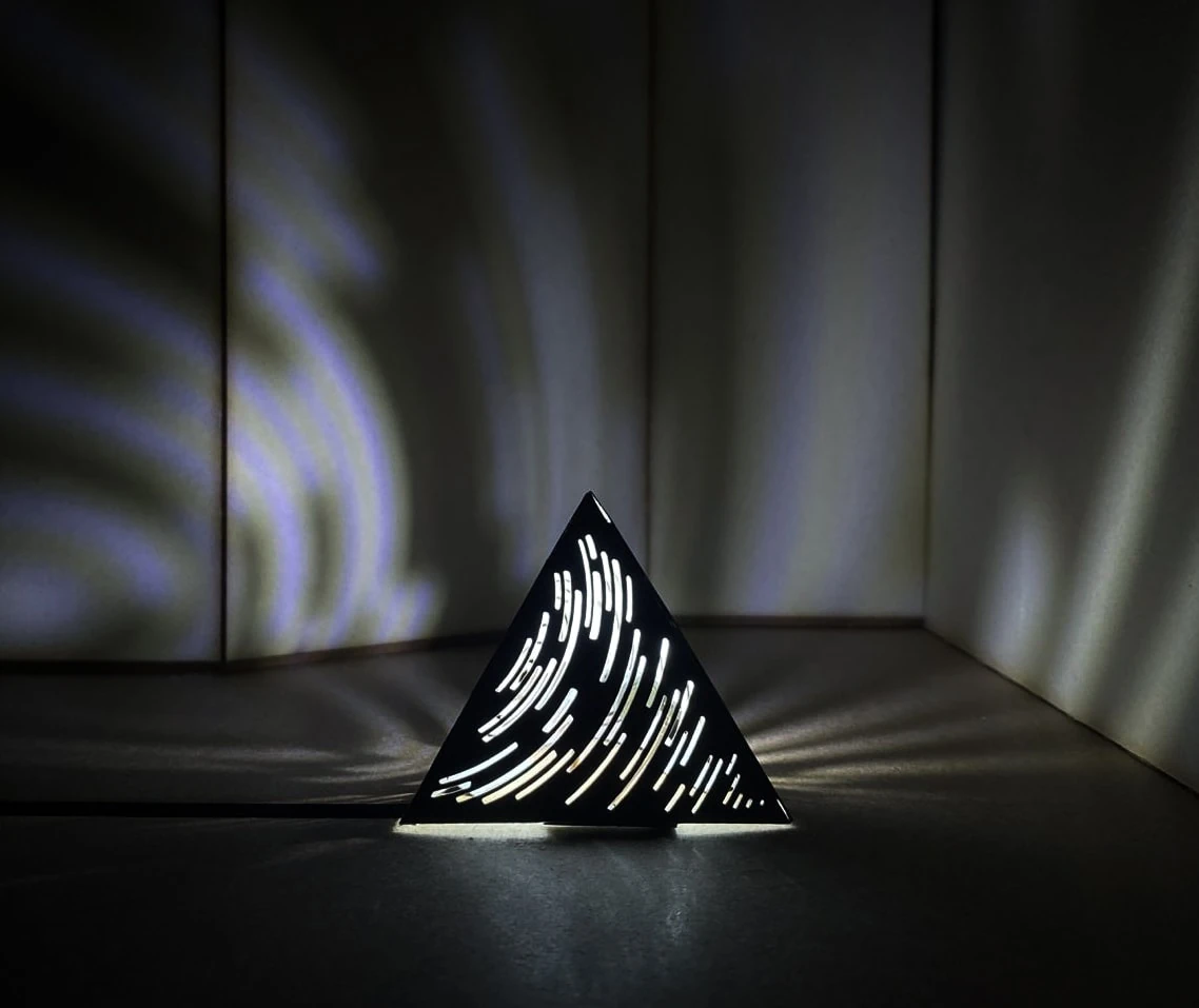 Maquette de la structure triangulaire ; ses fentes courbes projettent des ondes de lumière autour d’elle.
